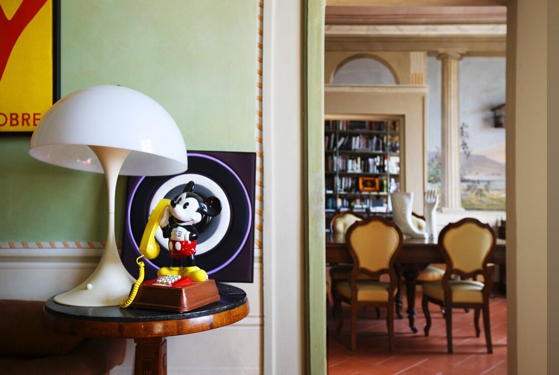 Mickey-Mouse-Figur und Vintage Leuchte auf Beistelltisch, daneben Blick in das Esszimmer mit Trompe L'oeil Malerei