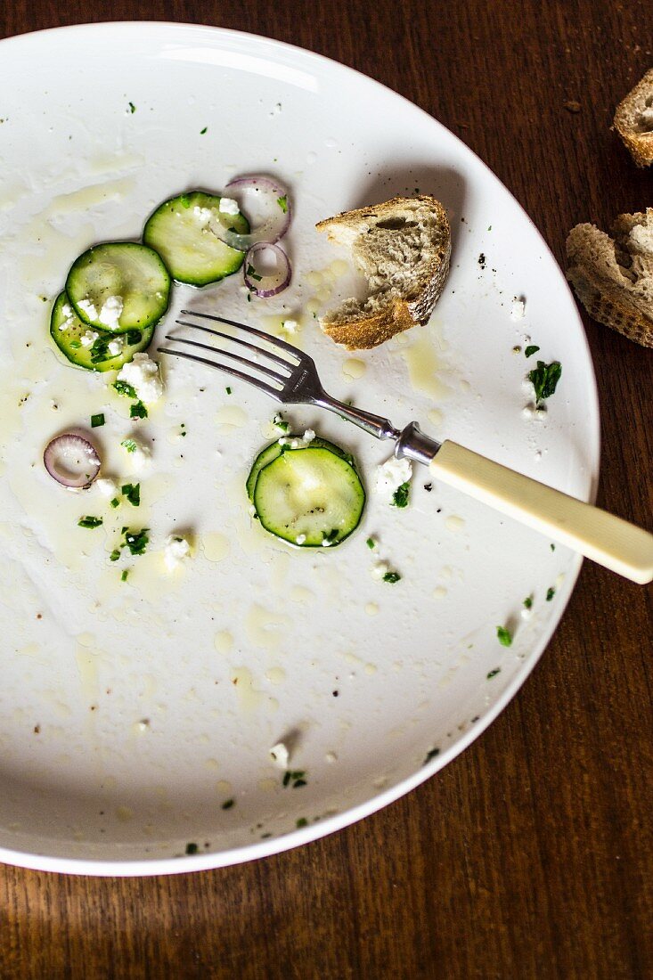 The remains of courgette carpaccio and bread on a plate with a fork