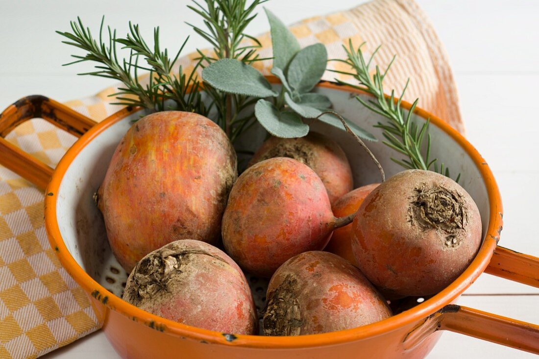 Golden beets in a colander with rosemary and sage