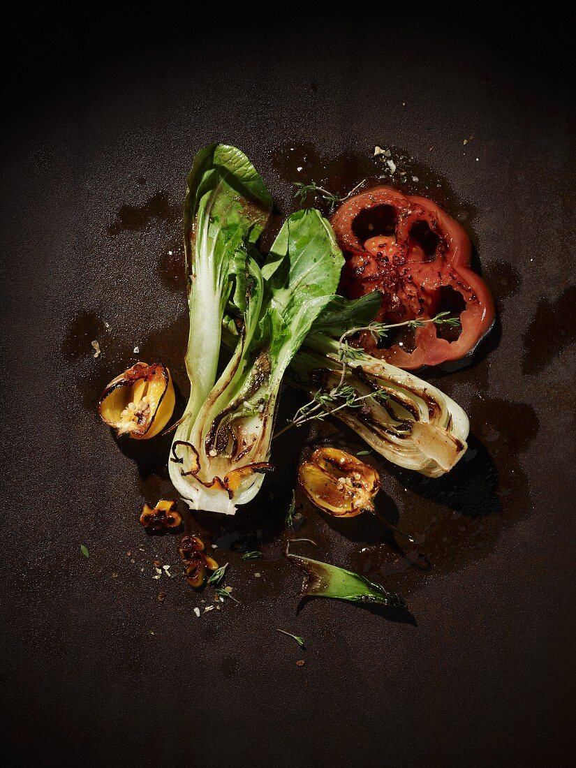 Grilled vegetables on a brown metal surface (bok choy, red peppers, halved, yellow habaneros) with a sprig of thyme