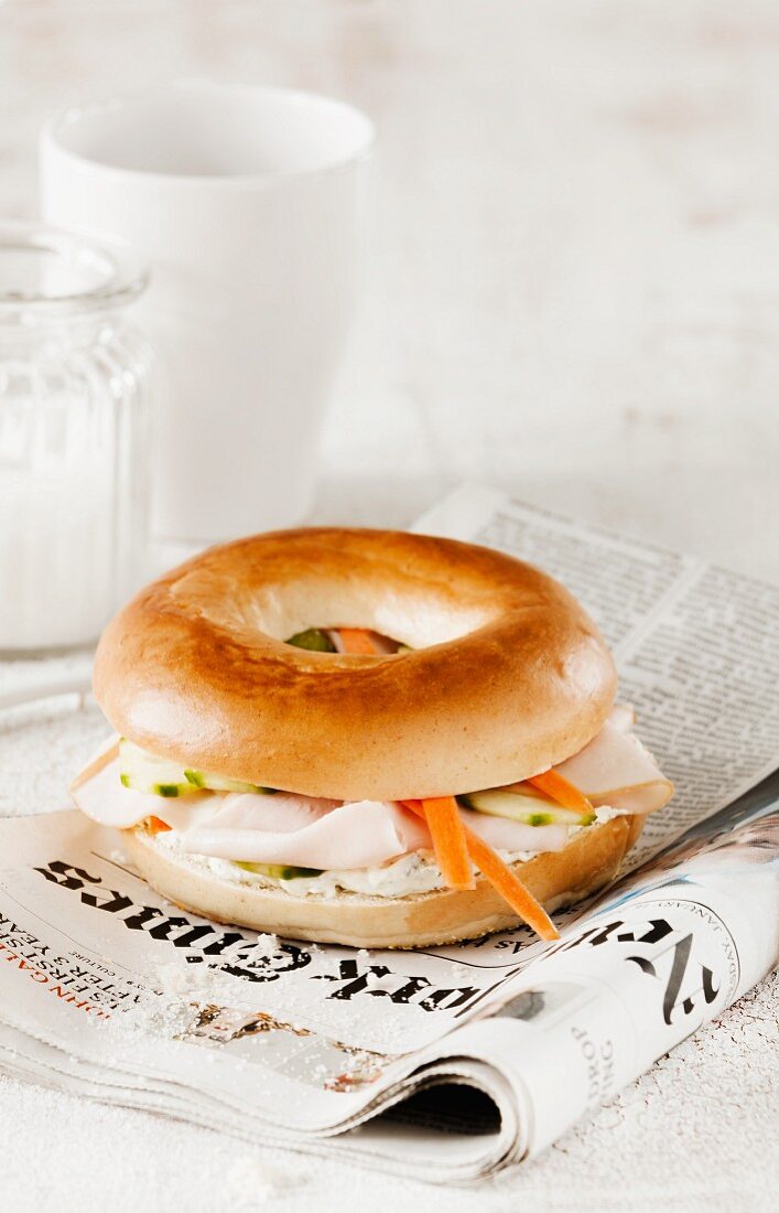 A bagel with turkey breast and carrots on a newspaper