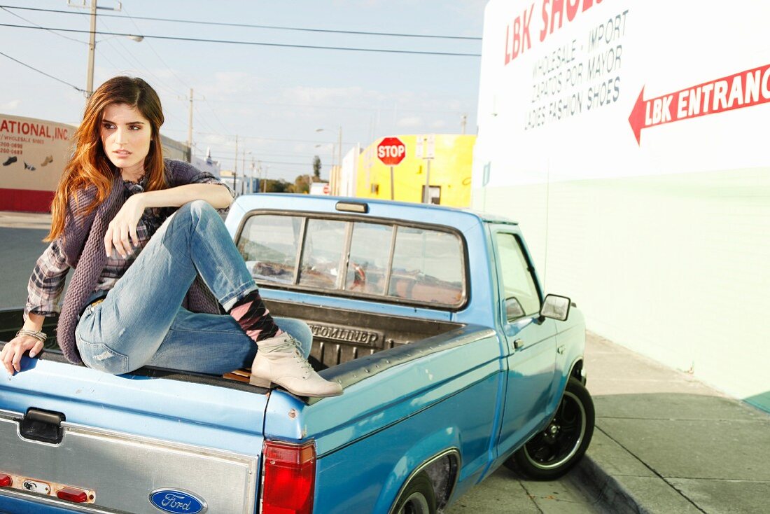 Junge, brünette Frau sitzt auf einem Pickup