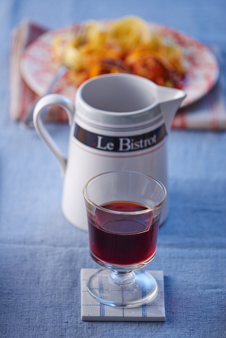 A glass of red wine with a pasta dish in the background in a bistro