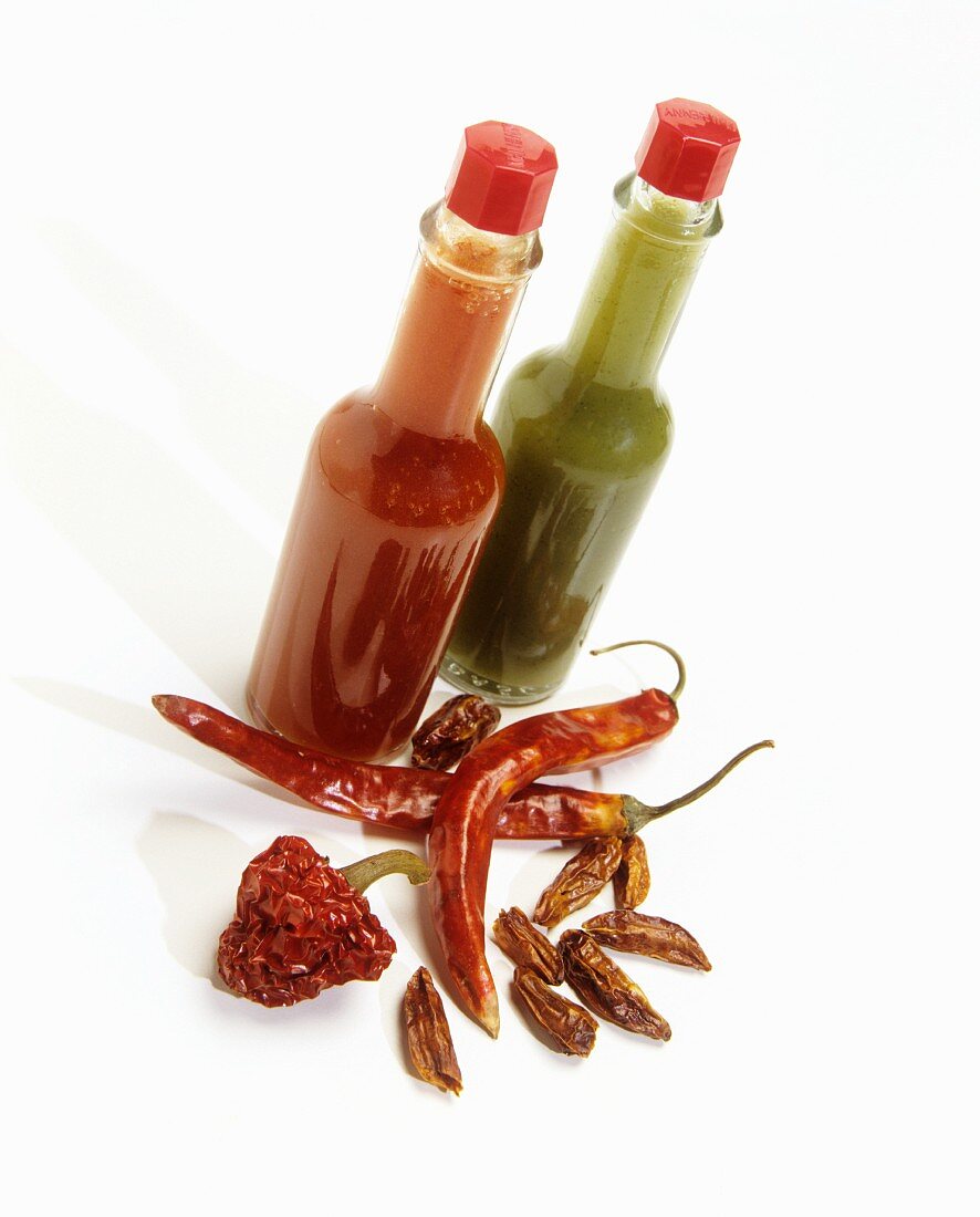 Rote und grüne Chilisauce in Flaschen und verschiedene getrocknete Chilischoten