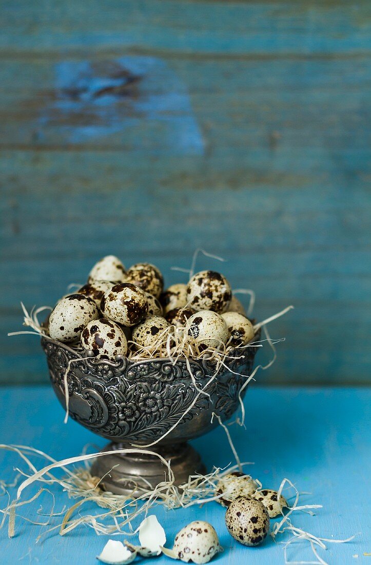 Quail's eggs with straw in a metal bowl