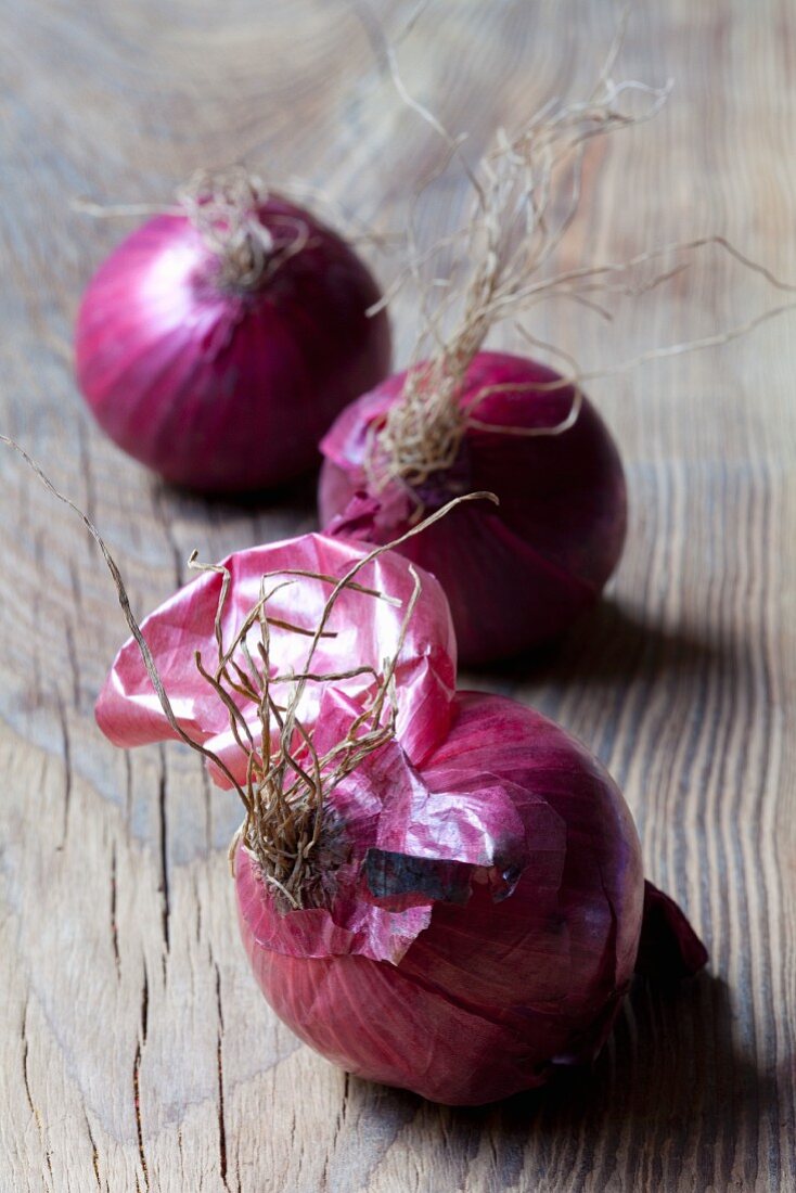 Three red onions on wooden background