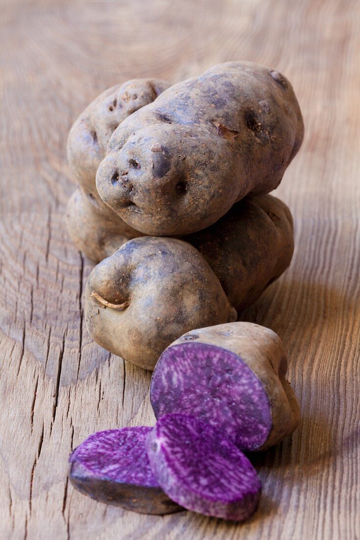 Purple potatoes, whole and halved, on a wooden surface