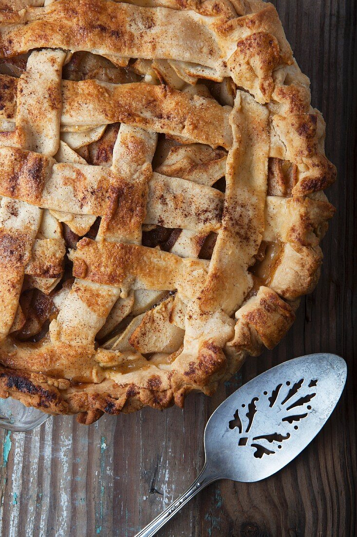 An apple pie on a wooden surface with a cake slice