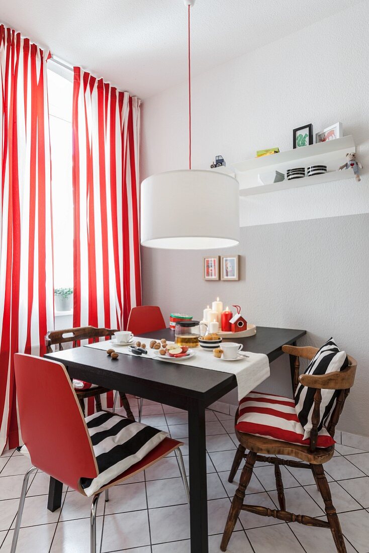 A dining area with old and new chairs against a window with red-and-white stripped curtains in a renovated kitchen