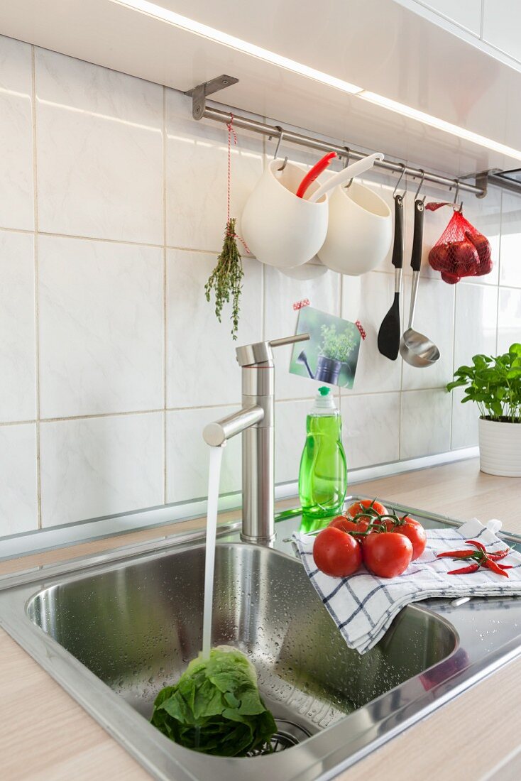 Edelstahl Spülbecken, darüber an Stange aufgehängtes Küchengeschirr in renovierter Küche