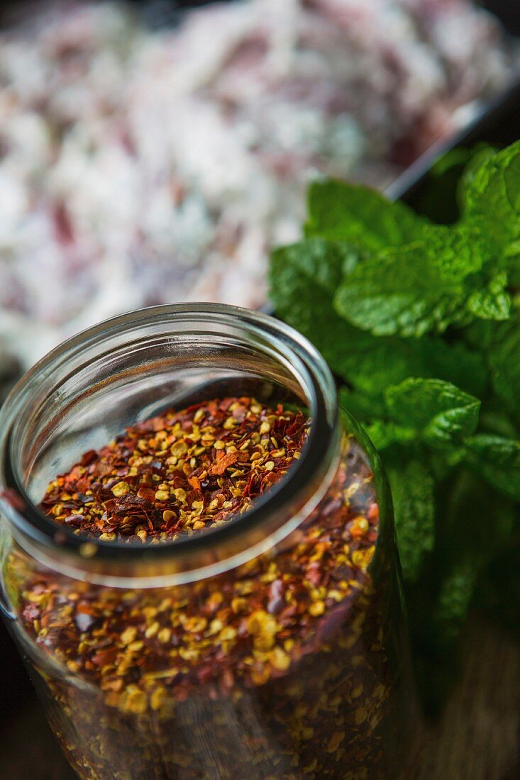 A jar of dried chilli seeds with fresh mint next to it