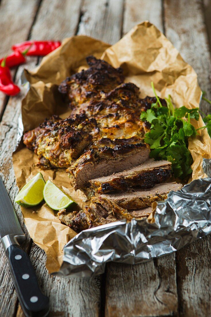 Roasted, sliced leg of lamb with coriander, chilli and lime on a wooden table