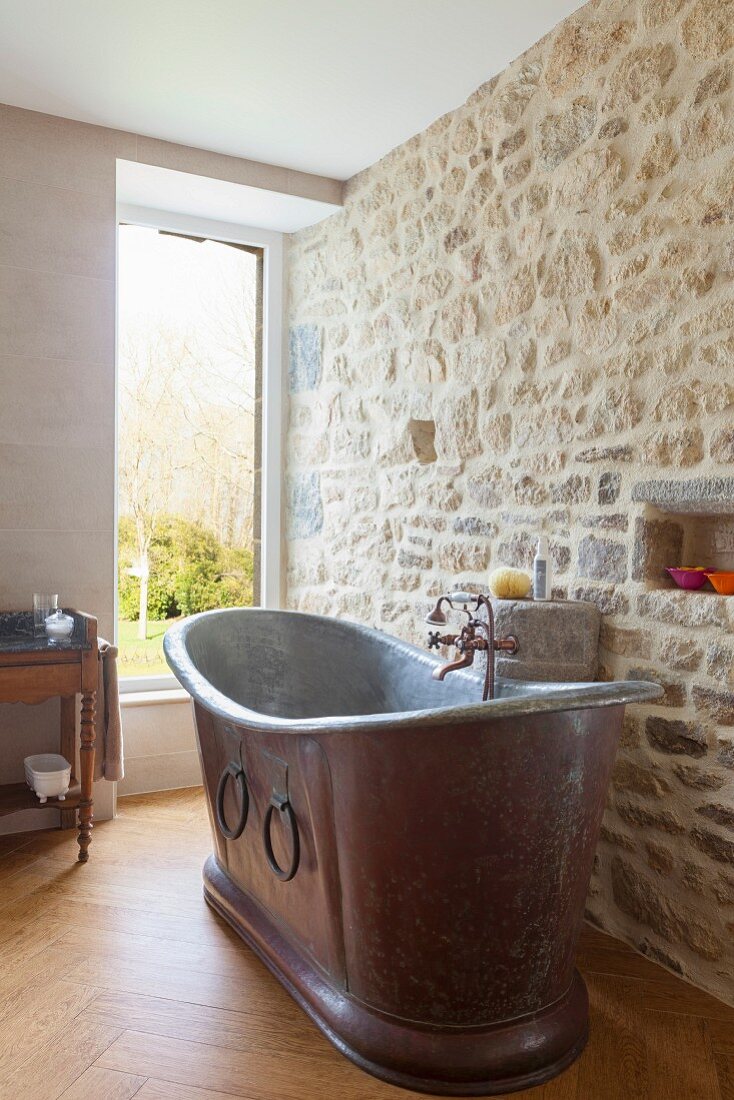 Vintage Metall-Badewanne vor Natursteinwand in renoviertem Bad mit Fenster