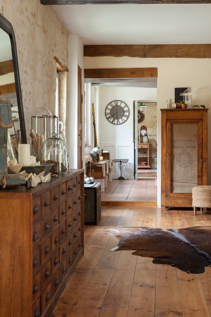 Animal-skin rug on wooden floor in rustic interior with stone wall, chest of drawers and view through open doorways