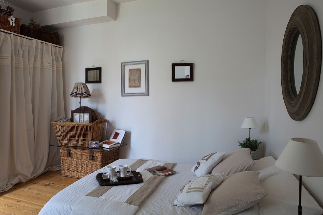 Double bed with pale bed linen, breakfast tray and wicker hamper in country-house bedroom