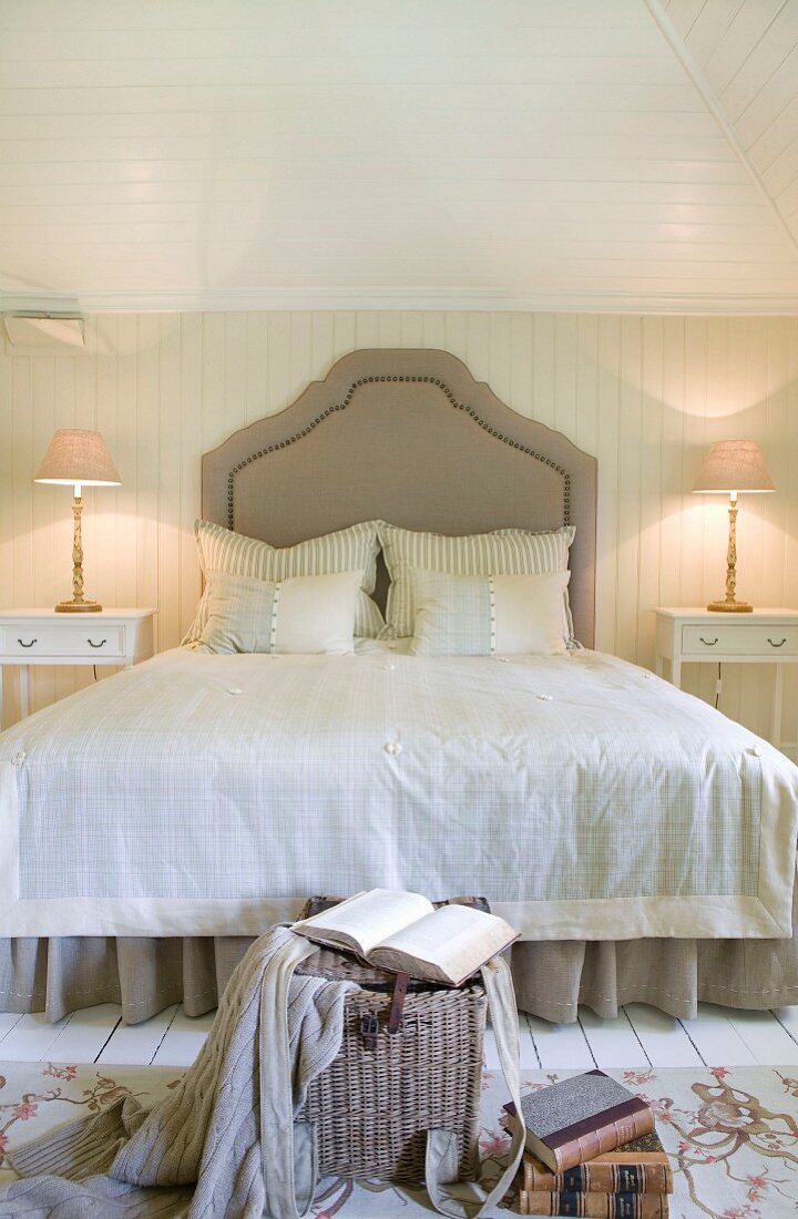 Grand double bed with curved headboard in country-house bedroom with pale wood panelling