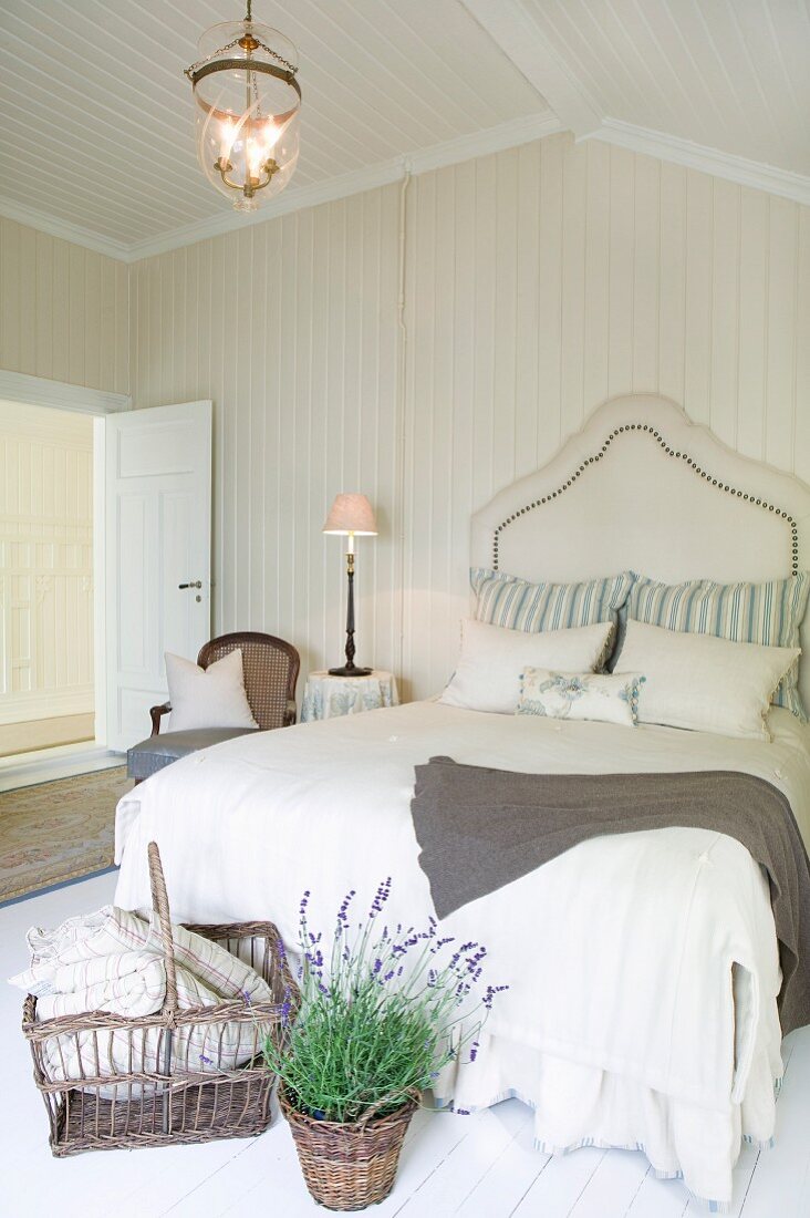 Korb und Lavendeltopf vor Doppelbett mit elegantem Kopfteil