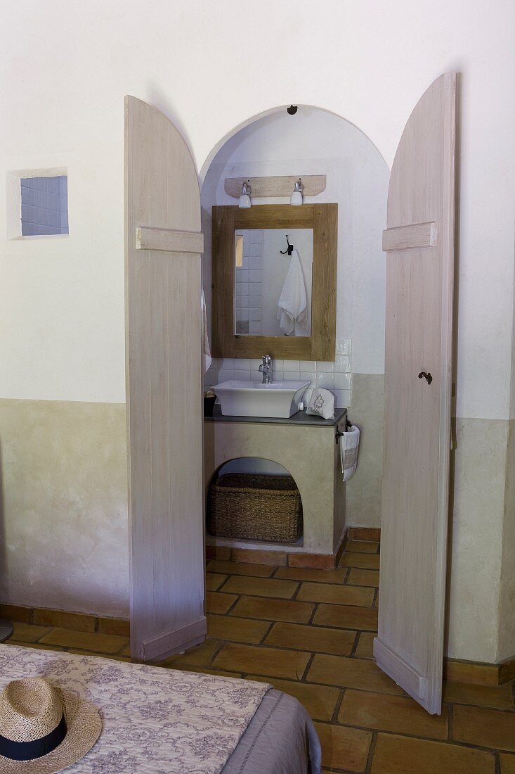Blick auf gemauerten Waschtisch in Bad Ensuite durch die geöffneten Flügeltür, Bettende mit floral gemustertem Überwurf