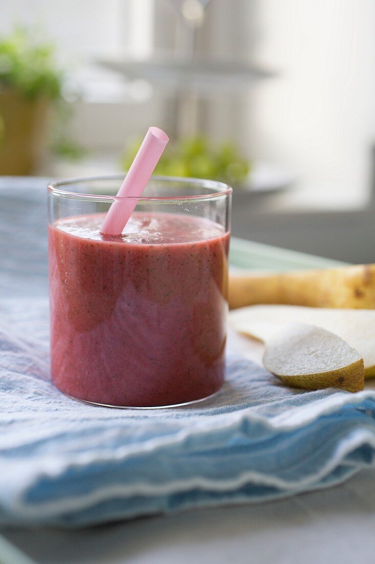 A red smoothie made with pears in a glass with a straw