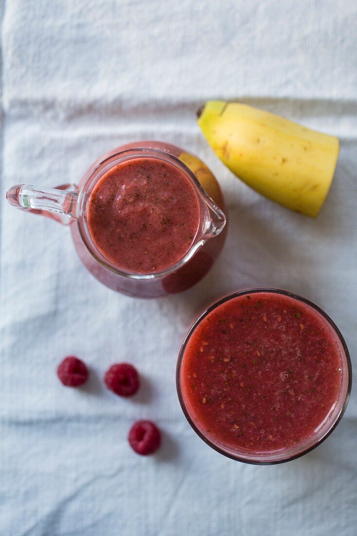 A banana and raspberry smoothie in a glass and in a jug