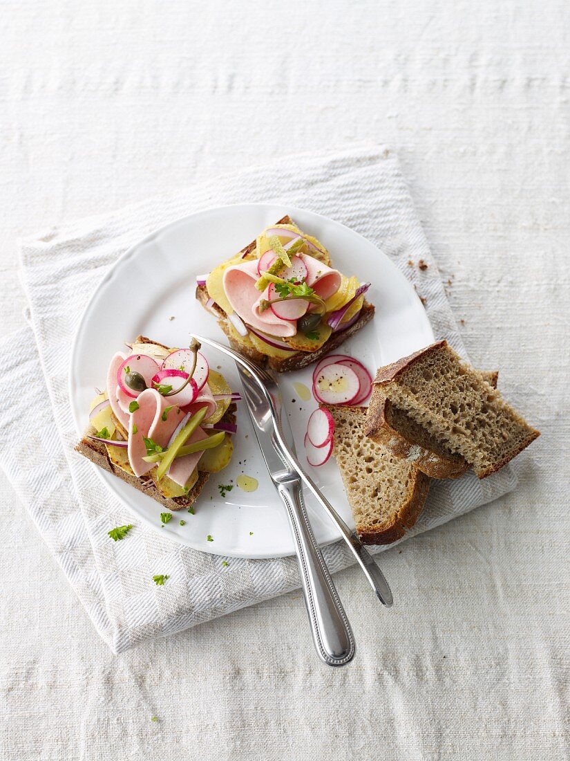 Slices of bread topped with potato salad, sausage and radishes
