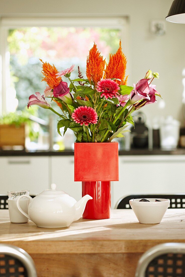 Blumenstrauss aus Gerbera und Calla in verschiedenen Rottönen in roter Vase auf Esstisch