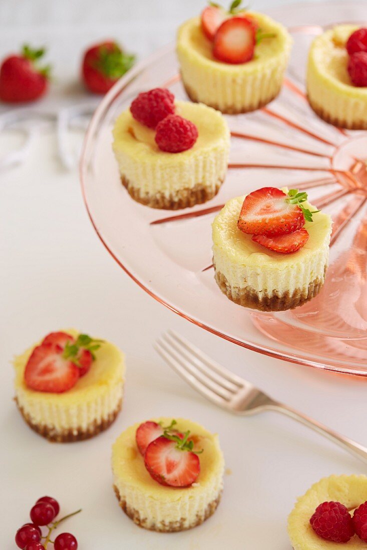 Mini cheesecakes with strawberries, raspberries and ginger biscuit bases on a cake stand