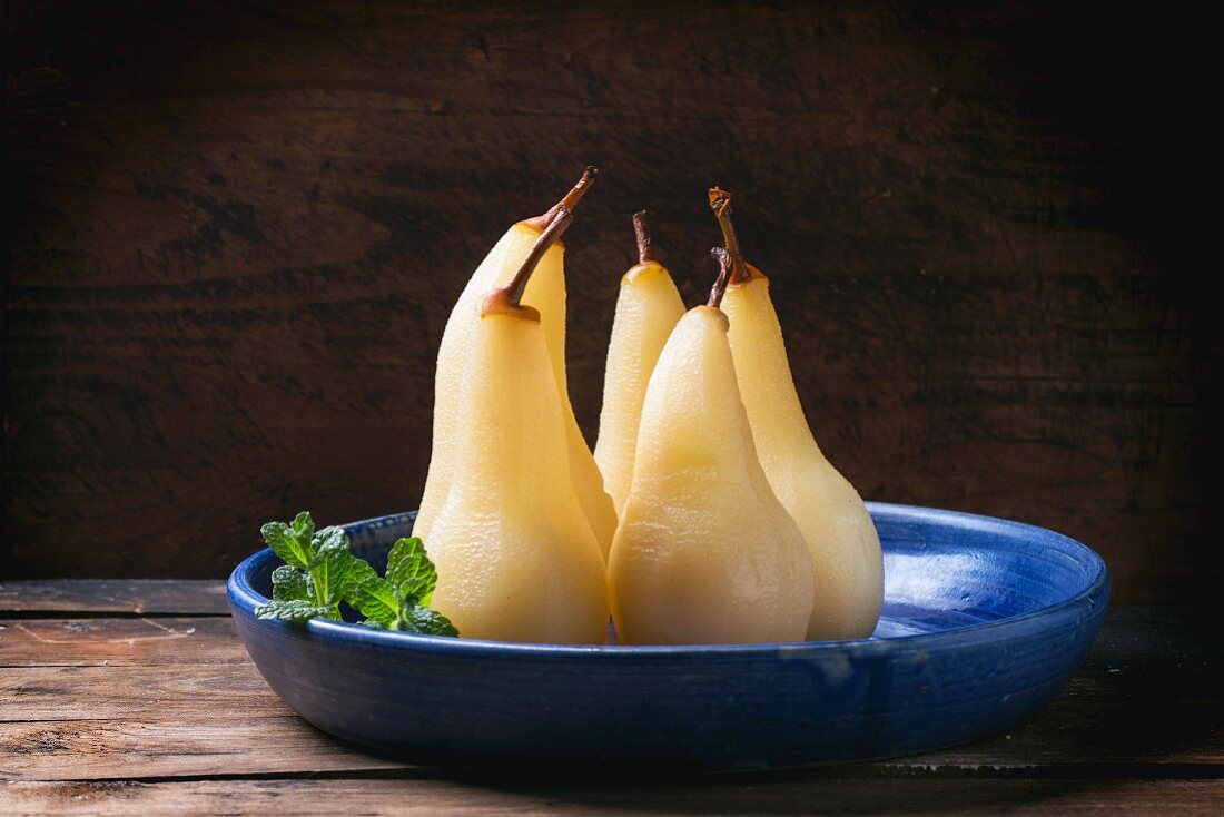 Pears poached in white wine with fresh mint in a blue ceramic dish