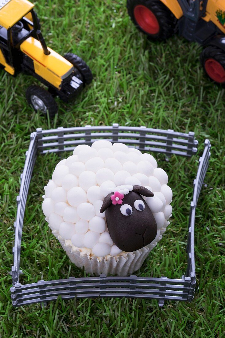 An Easter lamb cupcake and toy tractors on a grass surface