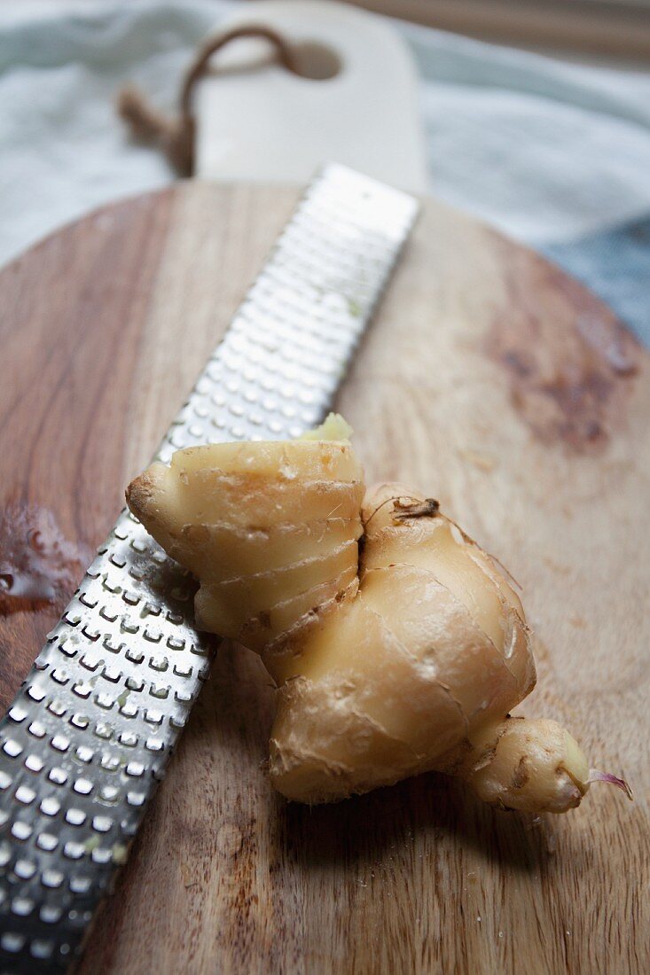 Fresh ginger root with a grater on a chopping board