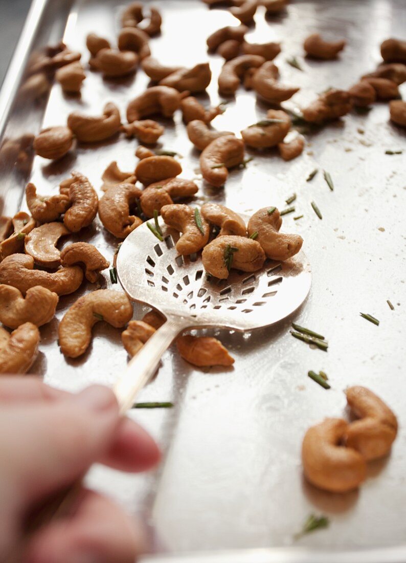 Cashew nuts with rosemary and a scoop on a baking tray