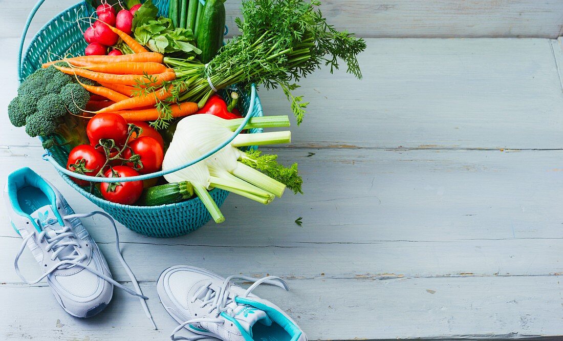 A shopping basket of vegetables with running shoes next to it