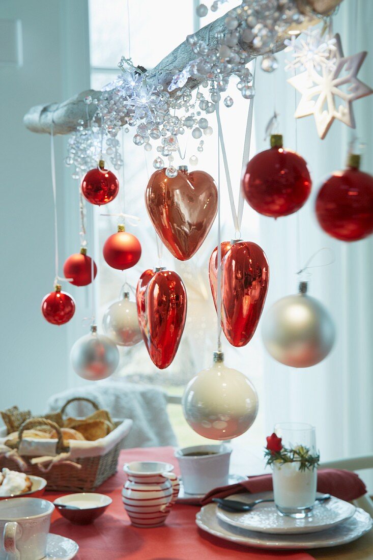 Hearts and Christmas tree baubles in red and white hanging on a branch over a breakfast table