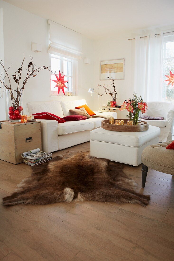 A country-style living room decorated for Christmas with red stars in the windows, a white two piece suite and an upholstered coffee table