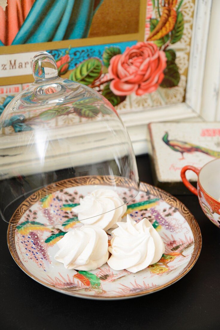 Meringues on a Chinese porcelain plate with a glass cloche and a picture of a saint in the background