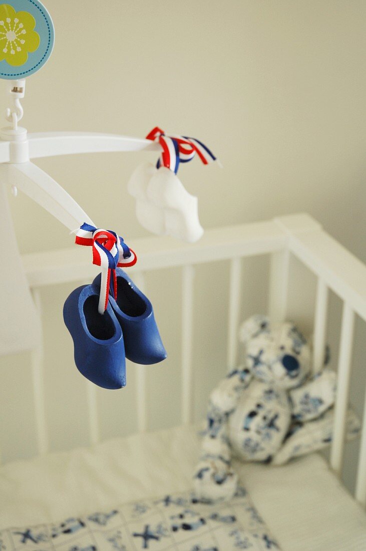 Hand-crafted mobile with miniature Dutch clogs above cot