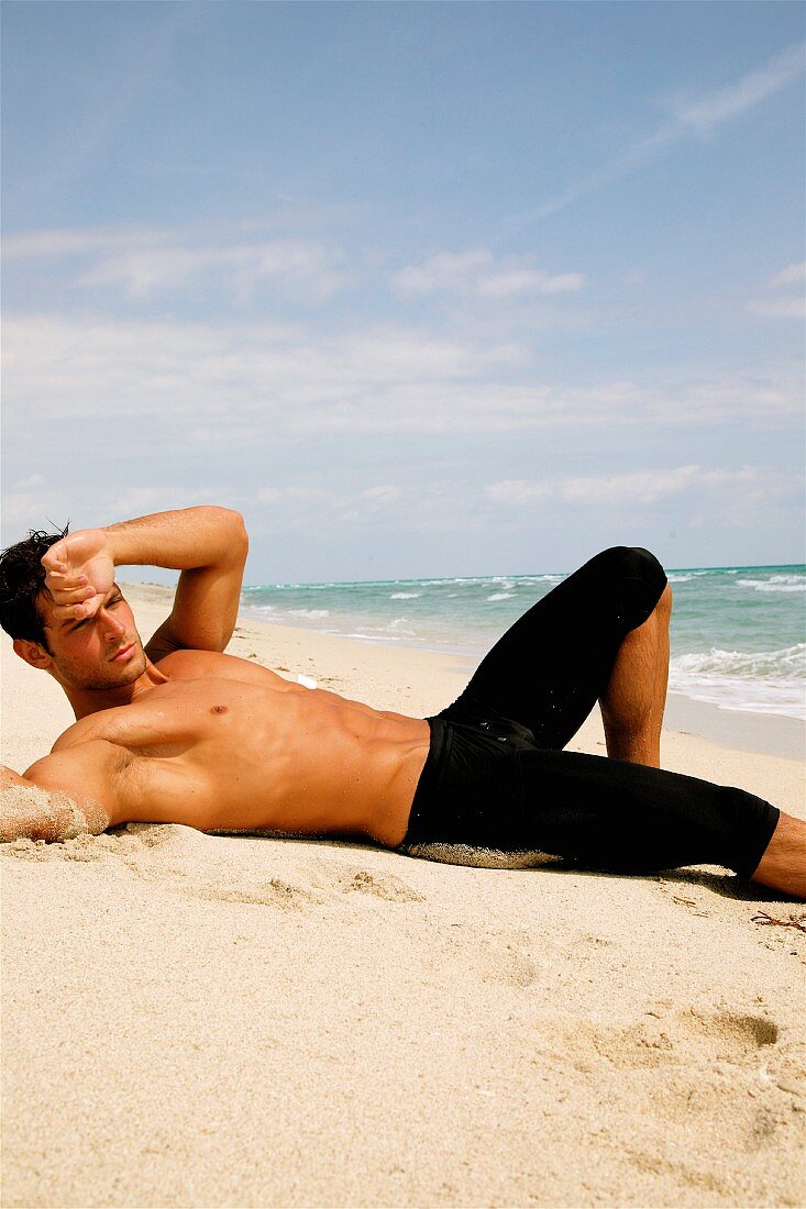 A sporty young man by the sea wearing black swimming trunks