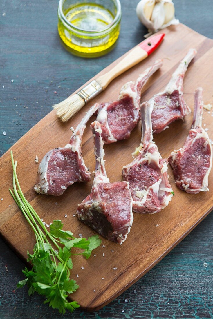 Raw lamb chops on a chopping board with garlic, olive oil and coriander next to it