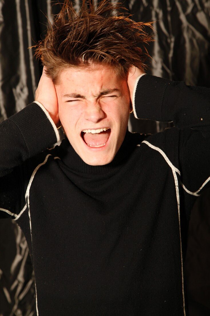 A young man screaming and holding his hands over his ears