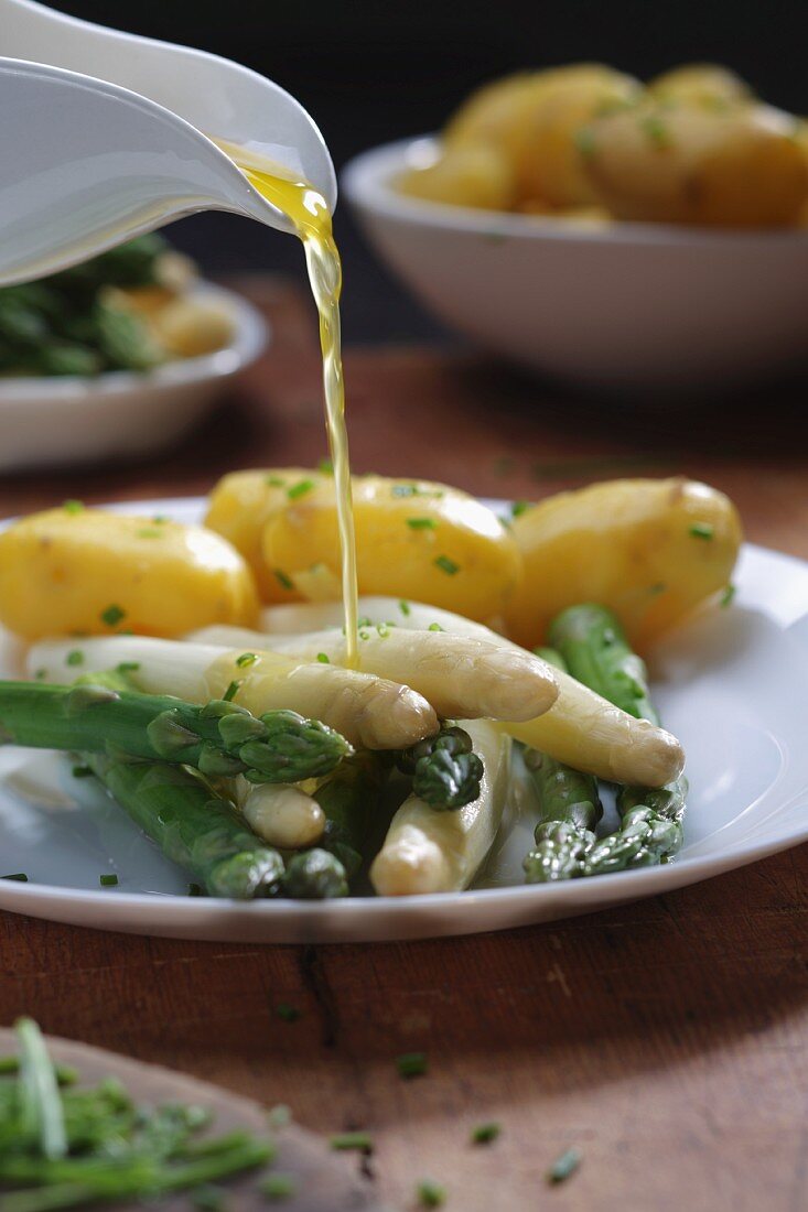 Melted butter being poured over asparagus with new potatoes