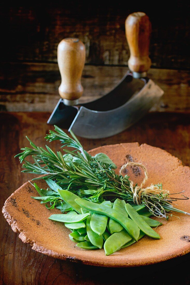 Mange tout and and bunch of herbs on a terracotta plate