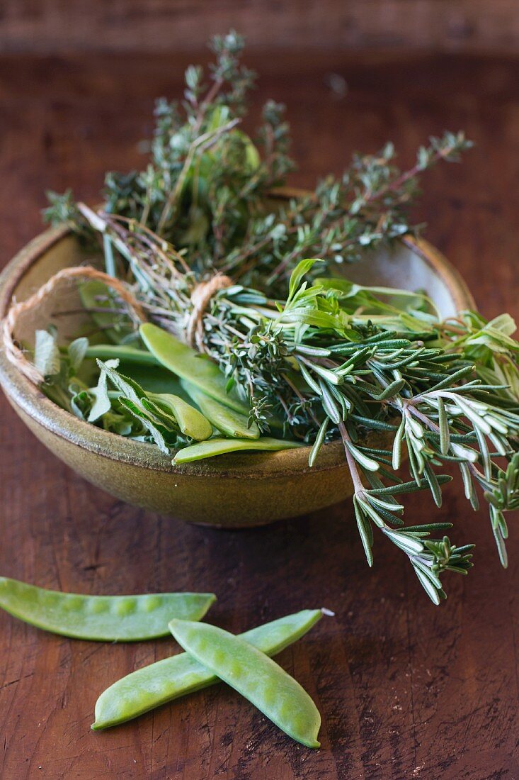 Mange tout and a bunch of herbs in a ceramic bowl