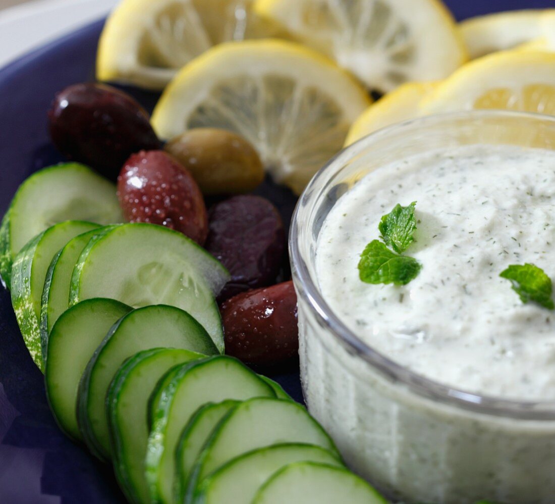 A bowl of tzatziki with cucumber, olives and lemon (close-up)