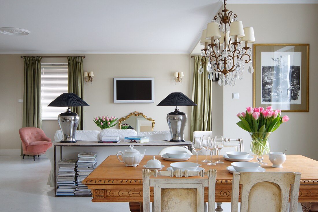 Vase of tulips on solid wooden table in front of sideboard against back of sofa in open-plan interior