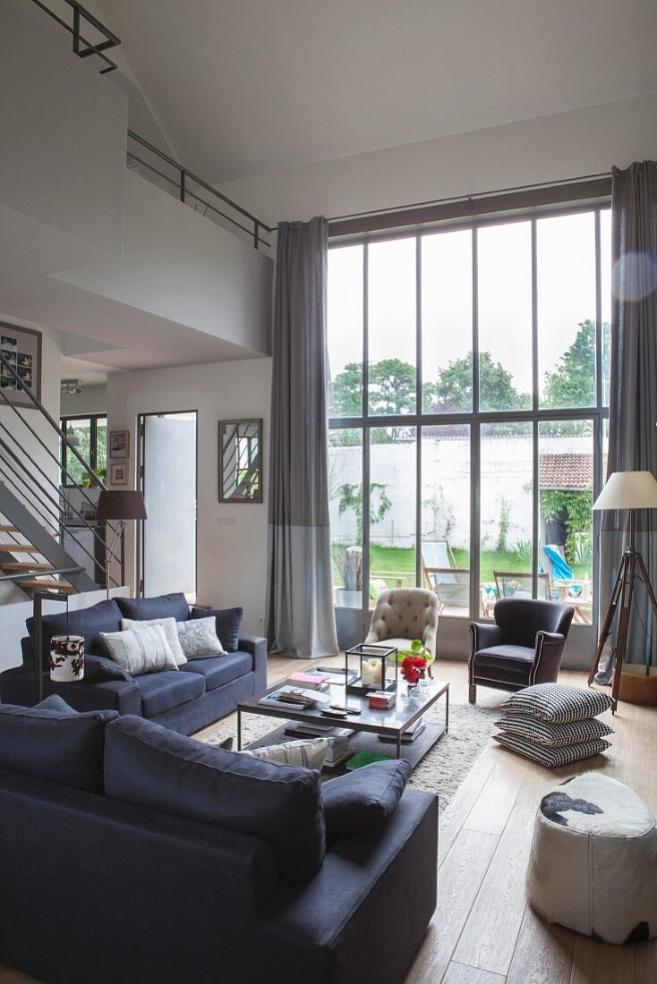 High-ceilinged lounge area in elegant shades of grey with glass wall leading to garden