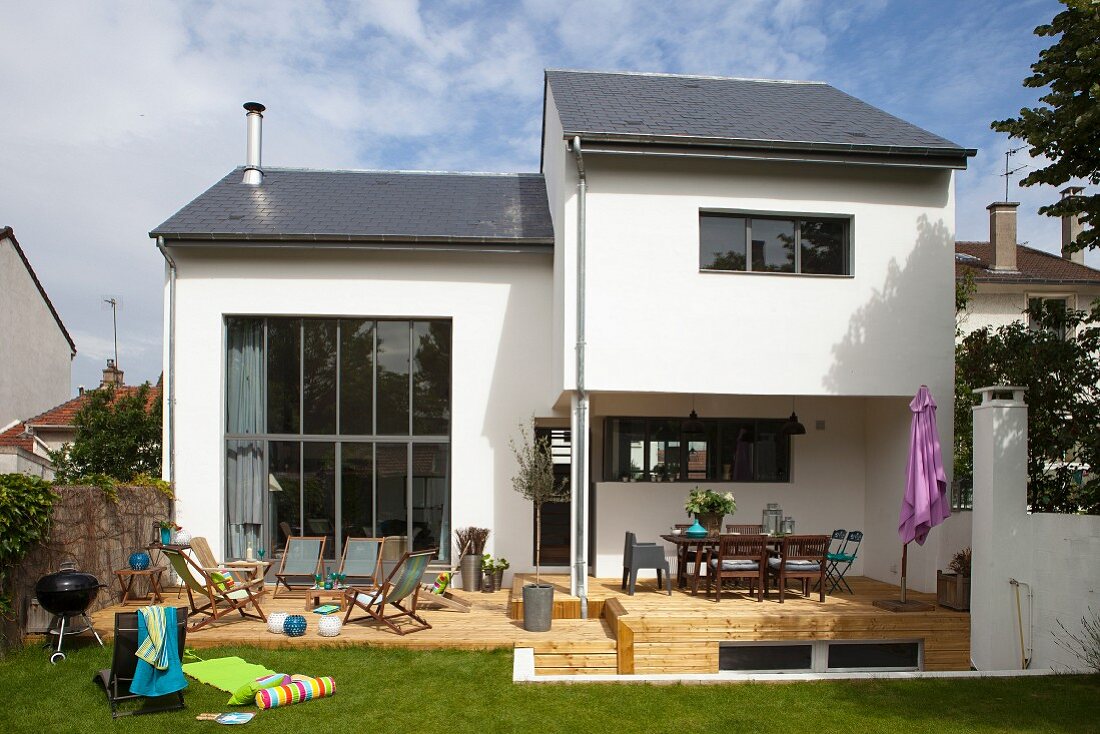 Modernes Wohnhaus mit naturbelassener Holzterrasse und Rasen in sommerlicher Stimmung