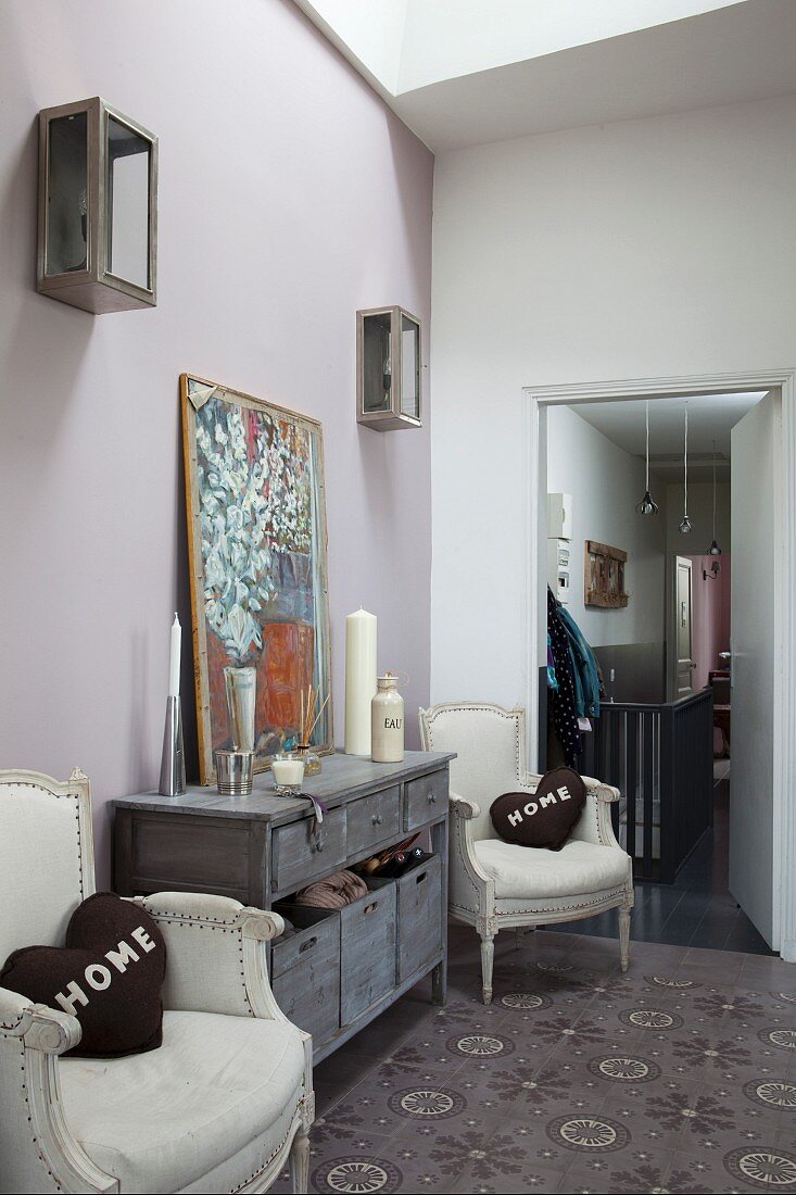 Chest of drawers flanked by two vintage armchairs with brown heart-shaped scatter cushions with 'HOME' lettering in foyer