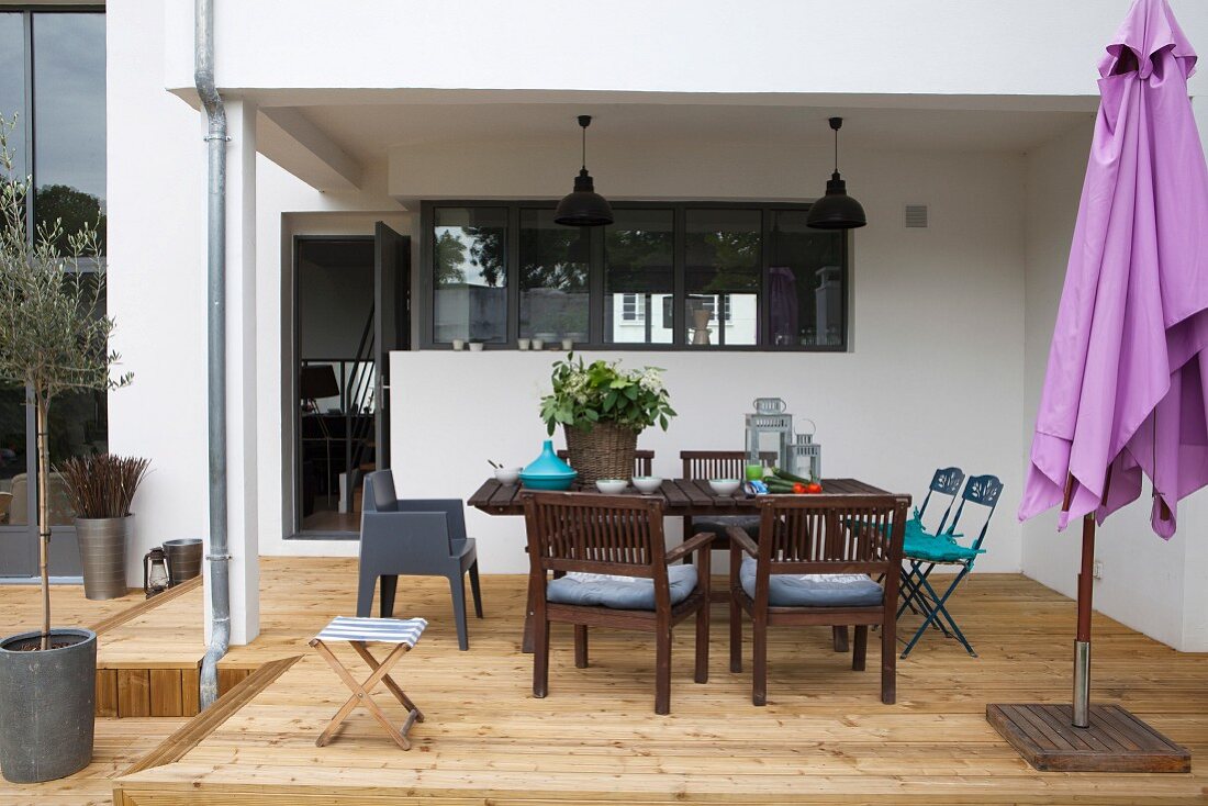 Outdoor furniture and purple parasol on roofed wooden terrace