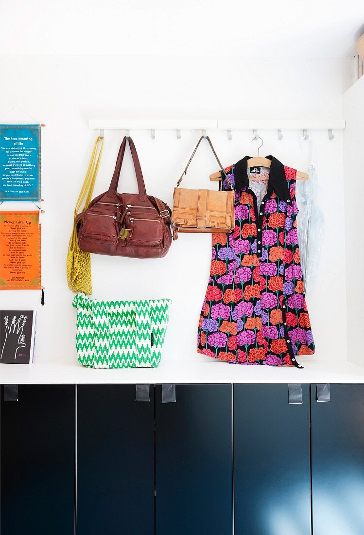 Leather bags and patterned tunic hung from wall hooks above cupboards with black fronts