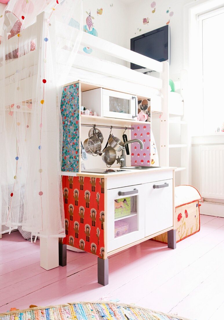 Tapezierte Kinderküche vor weißem Etagenbett mit Tüllvorhang auf hellem Dielenboden